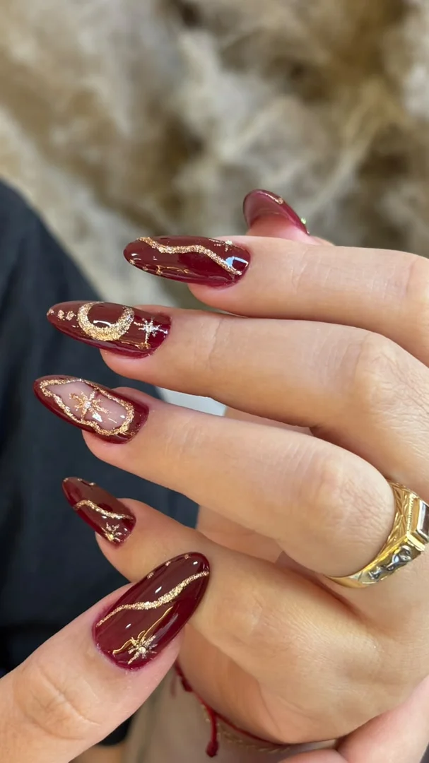 Unhas vinho com nail art de estrelas e lua douradas, trabalho da Terumi Nails