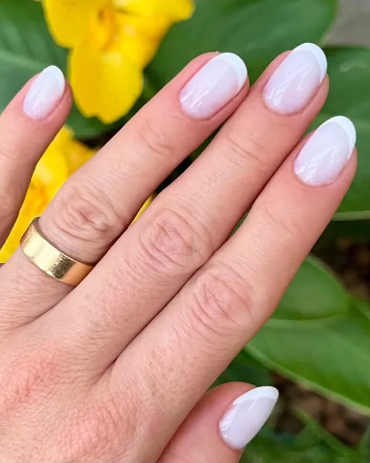 Mãos com unhas em gel branco leitoso entre flores amarelas, trabalho da Terumi Nails